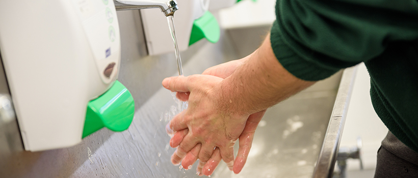 Male factory worker washing in hands under water in sink
